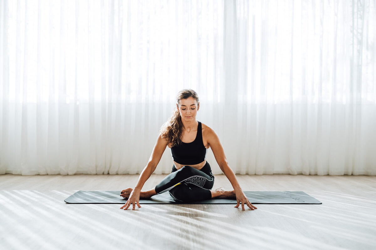 Woman sits happily in yoga pose at Upstate Studios, in light-filled space.